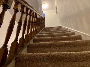 Stairs inside a house leading upwards to a landing and a light above.